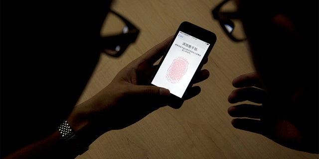 FILE - In this Sept. 11, 2013,  file photo, an Apple employee, right, instructs a journalist on the use of the fingerprint scanner technology built into the company's iPhone 5S during a media event in Beijing. The latest iPhones and Samsung Galaxy phones have fingerprint IDs that make it easier to unlock phones. Instead of typing in the four-digit passcode each time, you can tap your finger on the home button. (AP Photo/Ng Han Guan, File)
