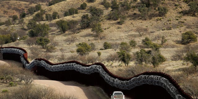 This March 2, 2019, file photo, shows a Customs and Border Control agent patrolling on the US side of a razor-wire-covered border wall along the Mexico east of Nogales, Ariz.