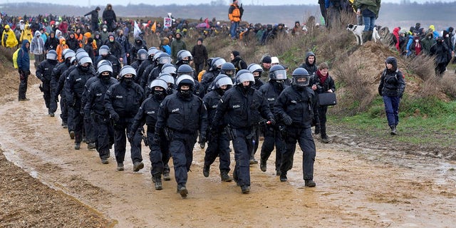 Police officers walk next to people who attend a protest rally at the Garzweiler opencast mining near the village Luetzerath in Erkelenz, Germany, Saturday, Jan. 14, 2023. 