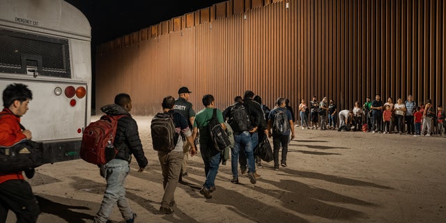 Immigrants wait to be processed by the U.S. Border Patrol after crossing the border from Mexico, with the U.S.-Mexico border barrier in the background, on Aug. 6, 2022, in Yuma, Arizona. 