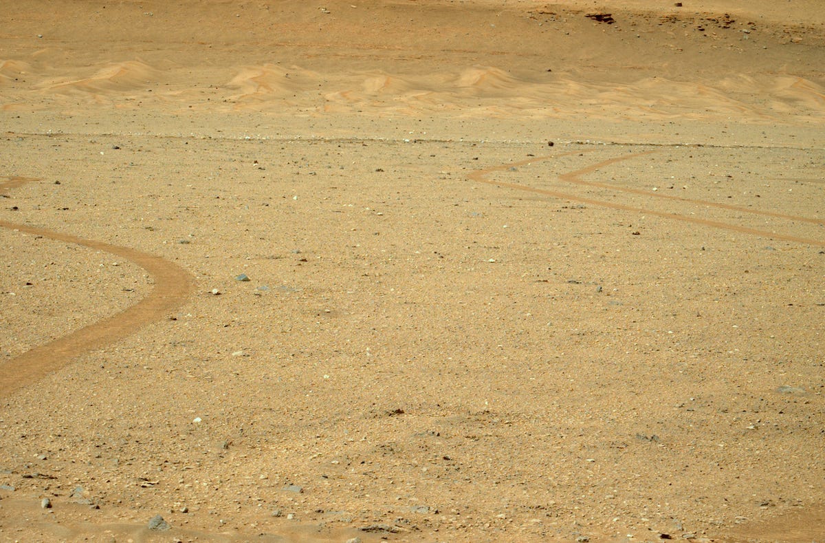 Large expanse of rocky, flat Martian landscape with a series of sand dunes in the distance.