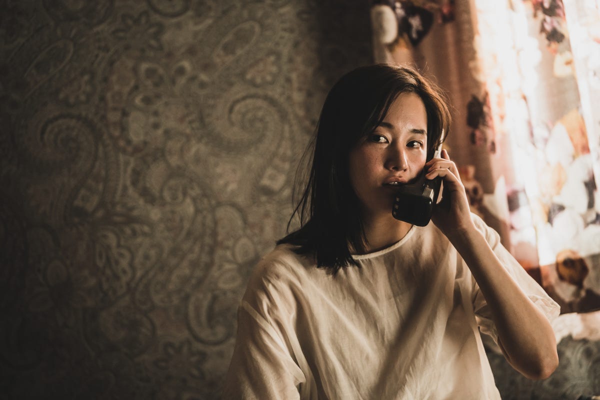 Jeon Jong-seo as Oh Young-sook inside her room, holding a phone. She's wearing a dirty frock