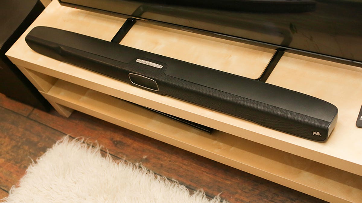 Looking down at a soundbar on a wood TV stands. There's a fuzzy white carpet.