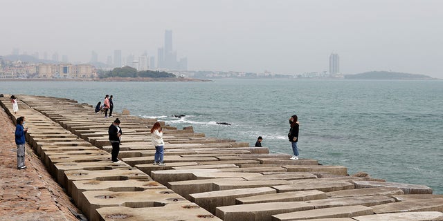A visitor poses for pictures on the coast of Qingdao, Shandong province, China, following an oil spill in the Yellow Sea caused by a collision between tanker A Symphony and bulk vessel Sea Justice off Qingdao port, April 29, 2021.