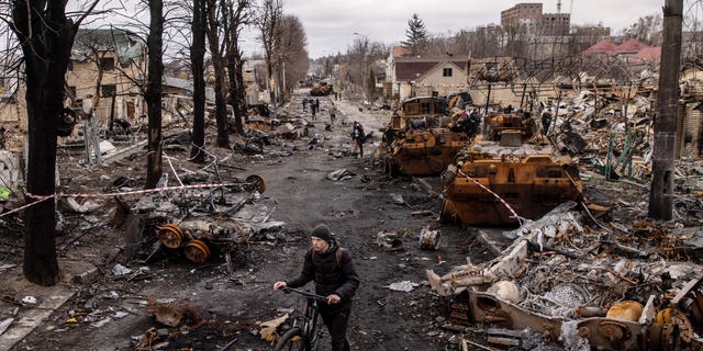 A man pushes his bike through debris and destroyed Russian military vehicles on a street April 6, 2022, in Bucha, Ukraine. 