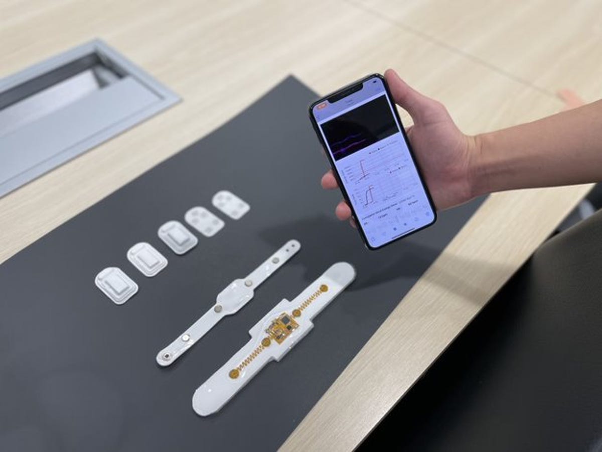 A smartphone is shown with the downloadable app for the system as well as the wristwatch and a few different chest-attachments.