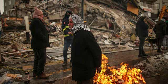 People warm themselves next to a collapsed building in Malatya, Turkey, on Feb. 7, 2023. Turkey will still hold its elections in May even after the devastating earthquake last month.