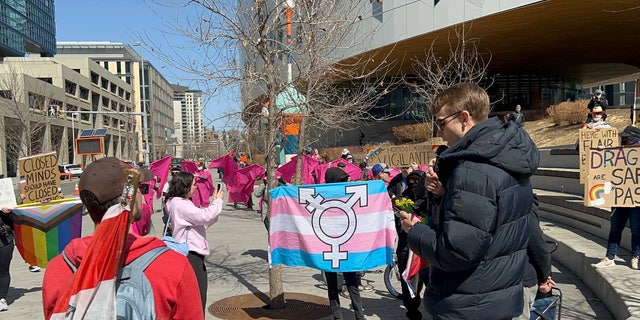Nathaniel Pawlowski reads from the Bible outside Calgary Public Library while protesters demonstrate with signs and a trans flag.