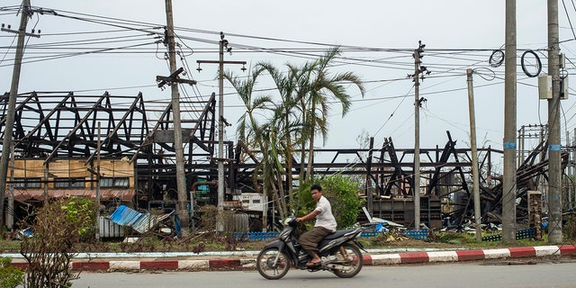 man rides motorbike past damaged buildings
