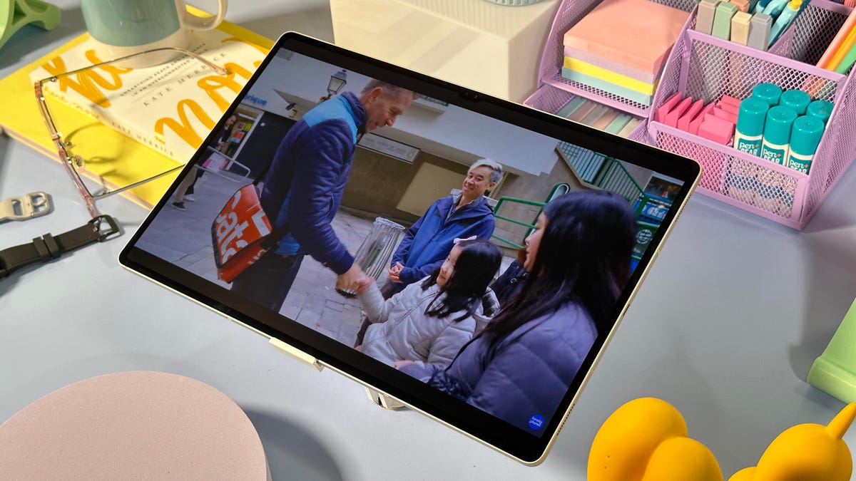 A travel video playing on a tablet sitting on a table covered in desk supplies.