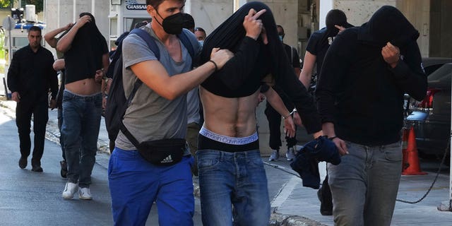 men cover their faces during police escort