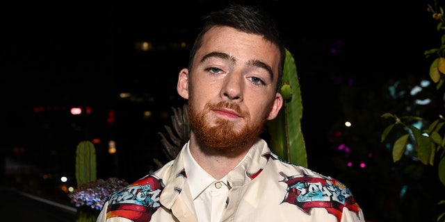 Angus Cloud in a patterned jacket looks at the camera