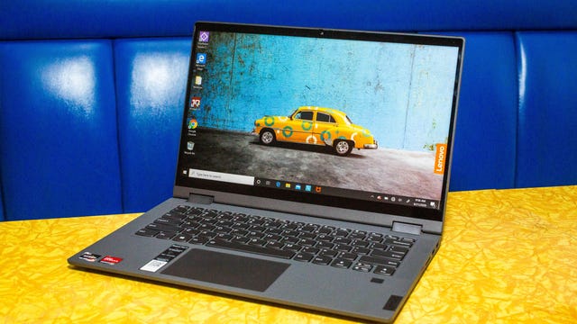 An open Lenovo Chromebook on a yellow tabletop against a blue background.