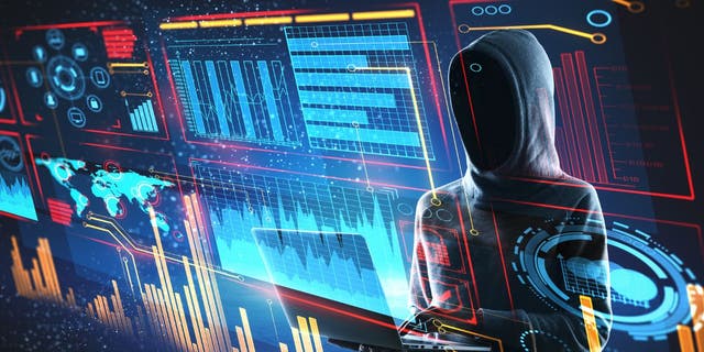 A hacker in a hoodie, face not shown, pulling up data on a laptop