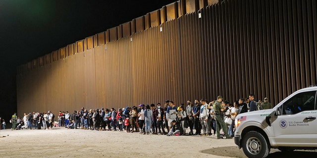 Migrants standing in a line along the border wall