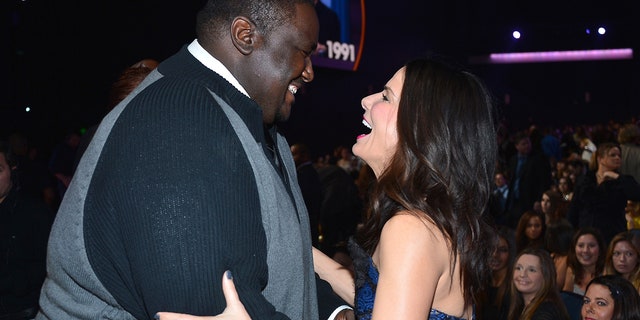 Quinton Aaron looks down at Sandra Bullock as she grabs his arms and laughs upward at the People's Choice Awards