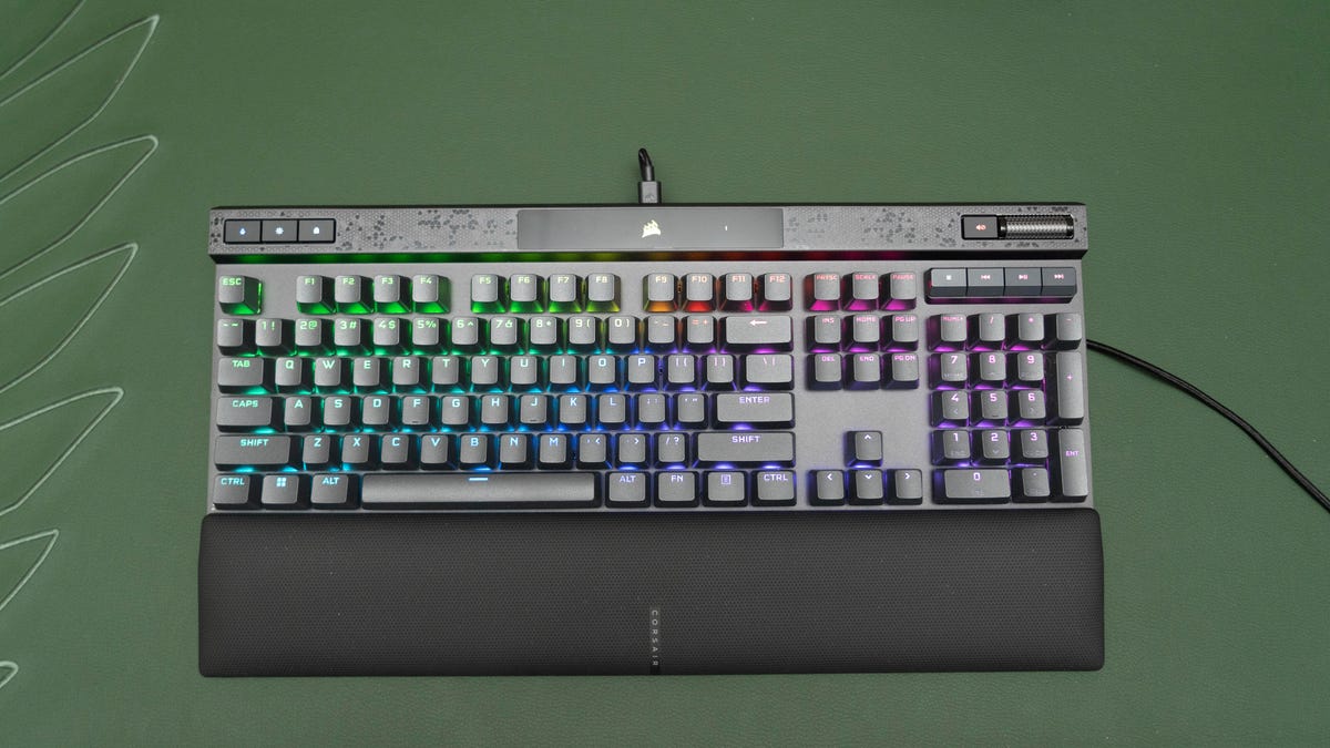 The Corsair k70 Max on a green background shown from directly above. There's a wristrest attached and has rainbow lighting