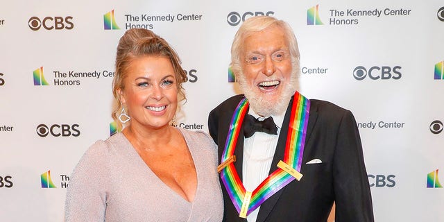 Dick Van Dyke in a tuxedo and rainbow medal smiles with his wife Arlene in a light purple dress