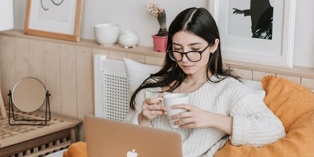 Woman sipping coffee while looking at her laptop.