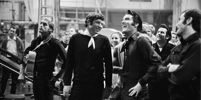 Steve Binder wearing all black and Elvis Presley wearing all denim as they look up and laugh