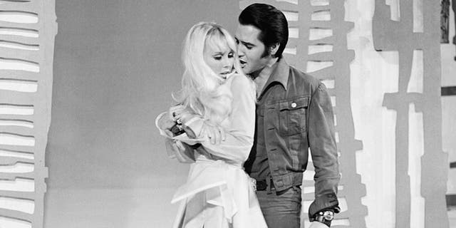 Susan Henning in a tiny white dress being held by Elvis Presley in a denim suit