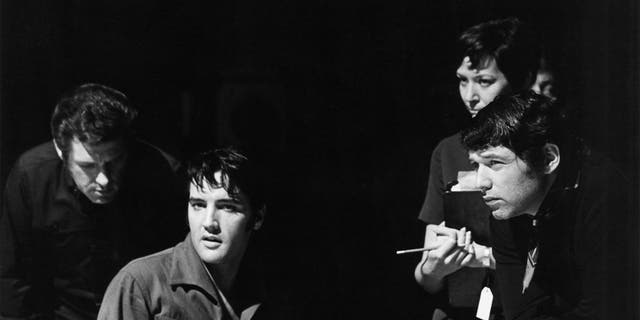 Elvis Presley looking away as he suits next to several men on stage
