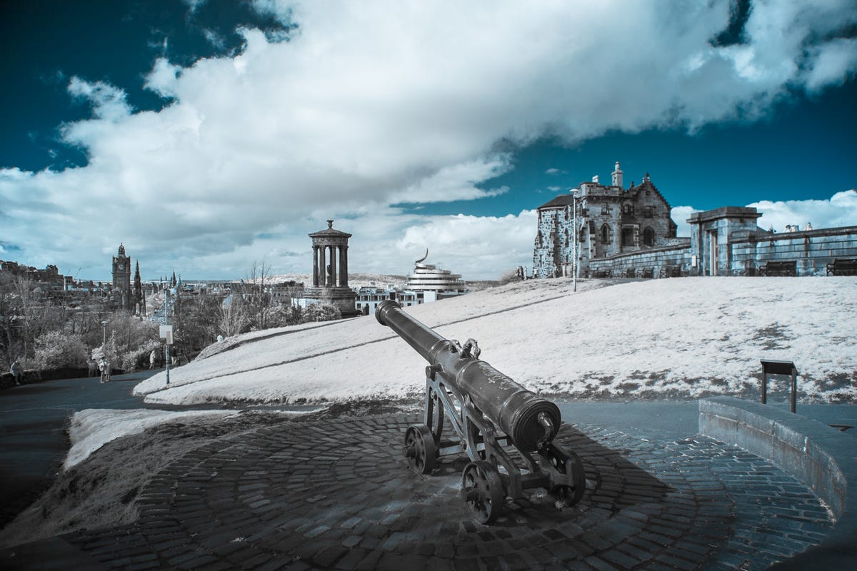 An landscape image showing a cannon and a building under blue sky.