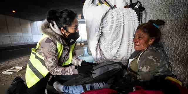 San Bernardino Mayor handing homeless woman under bridge a care package.