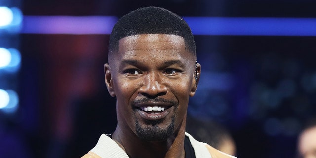 Jamie Foxx in a yellow jacket with white trim smiles on the set of "BEAT SHAZAM"