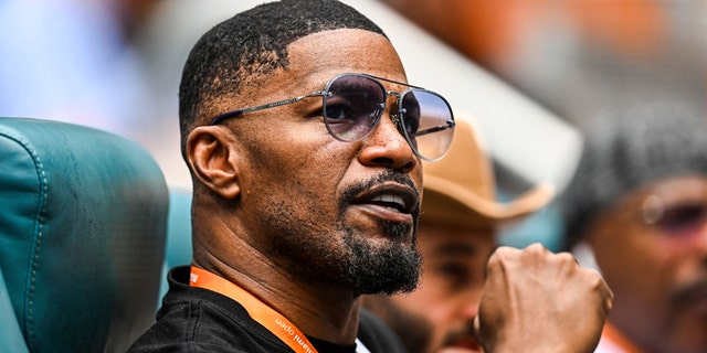 Jamie Foxx pumps his fist in the air while watching tennis