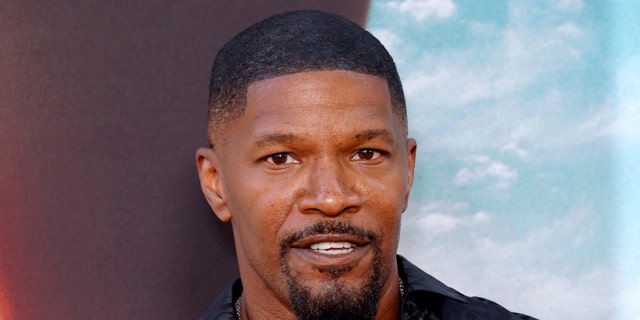 Jamie Foxx smiles on the red carpet in a black shirt