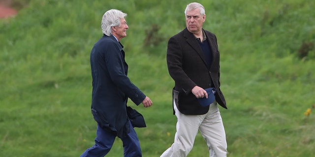 Prince Andrew in a black blazer and white slacks talking to Paul Tweed in a navy coat and blue jeans in a field