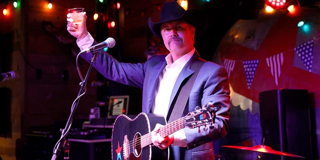 John Rich holds whiskey glass in the air with guitar strung around his neck at Nashville bar