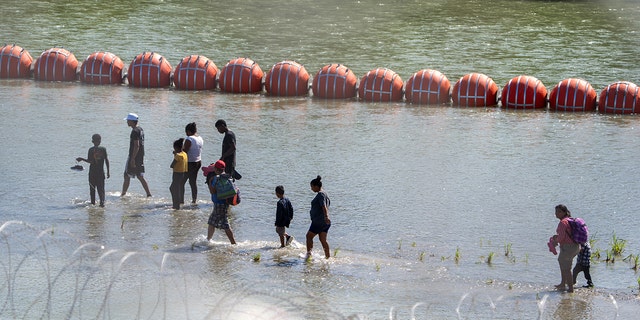 Migrants walk near the floating barrier in the Rio Grande