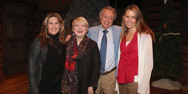 Wendi Lou Lee wearing a red vest and a white sweater posing with castmates of Little House