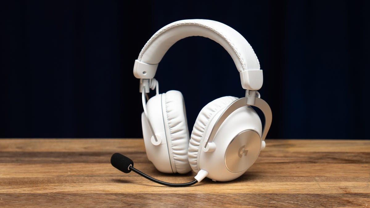 A white Logitech G Pro X 2 standing upright on a wood surface against a blue background with the earcups tilted away from you