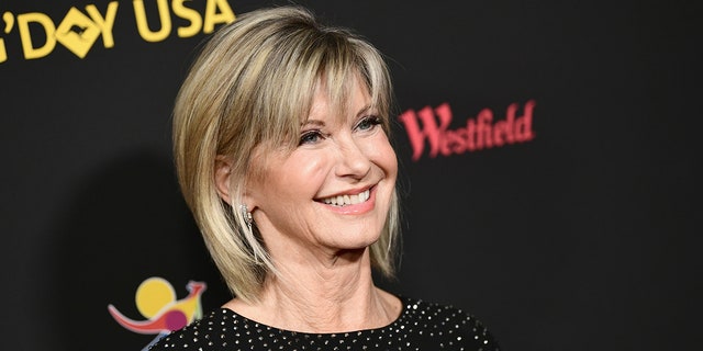 Olivia Newton John smiles and looks up on the carpet