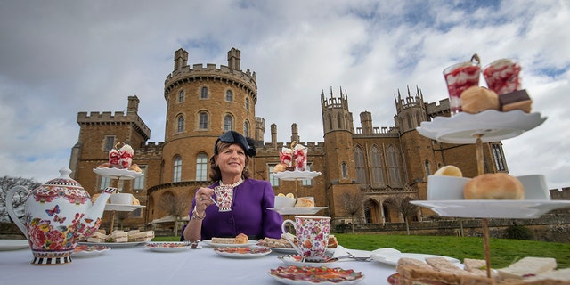 Emma Manners wearing a purple dress with a matching hat having tea outside Belvoir Castle