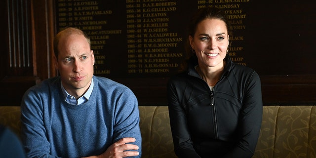 Prince William in a baby blue swearter sitting next to Kate Middleton in a hunter green jacket