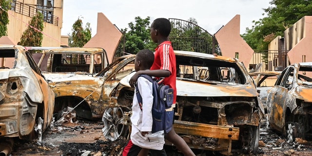 burned out cars on street as children walk by
