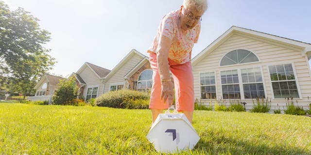 Susie is bending down to pick up her Wing delivery service order in her front yard