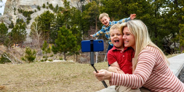 A mother poses for a selfie with her two sons with Mt. Rushmore in the background