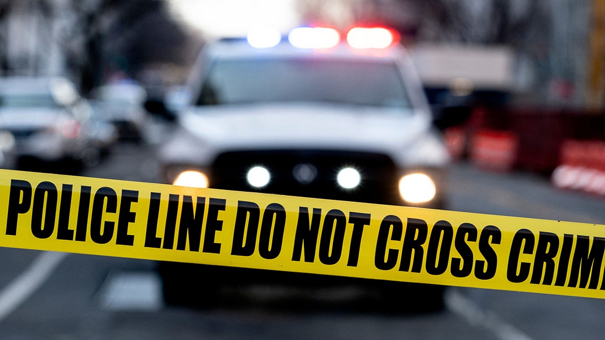 Police tape is pictured with blurred police vehicle in background