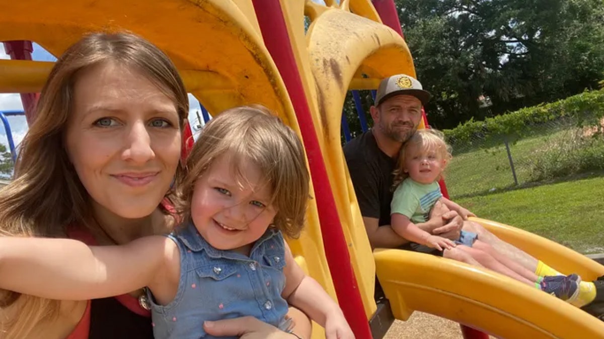 Mom smiling and holding her daughter in a playground next to a father smiling and hold his son.