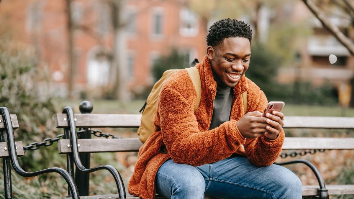 Man sitting on a park bench, smiling at his phone.