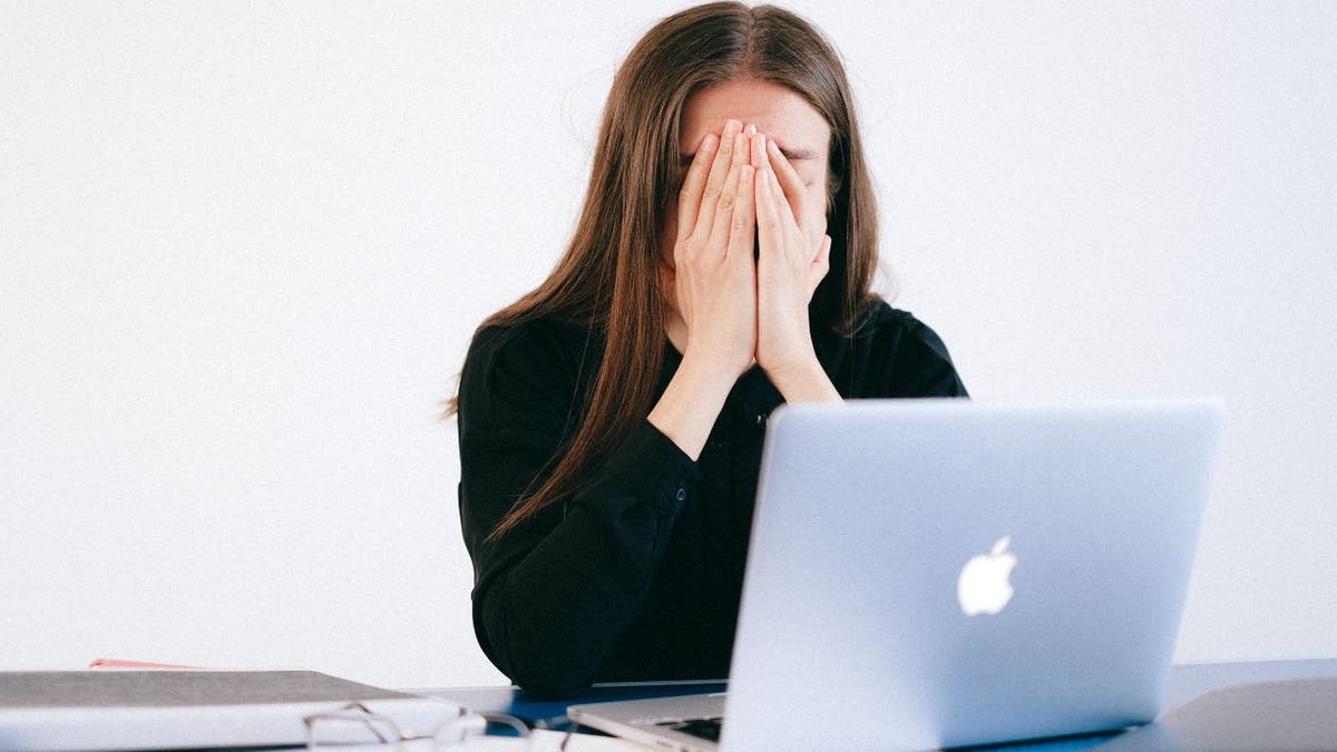 Woman sitting at her laptop with her hands over her face.