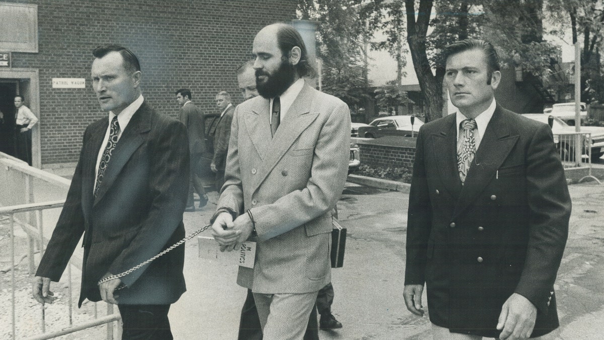 Leaving police headquarters today for his extradition hearing, Karleton Armstrong is led by Constable Ken Greer. Armstrong is wanted in Wisconsin in bombing of a university building in which a scientist was killed.