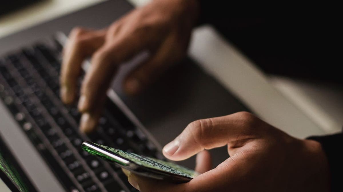 hands on laptop keyboard while holding phone