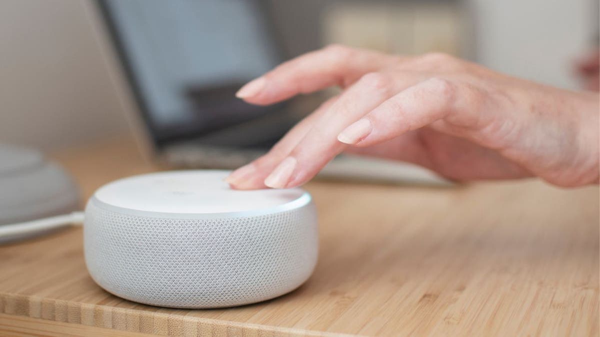White Amazon Echo device on a light wooden table with a hand touching the device
