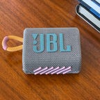 Small JBL Go 3 speaker resting on a table near a stack of books.